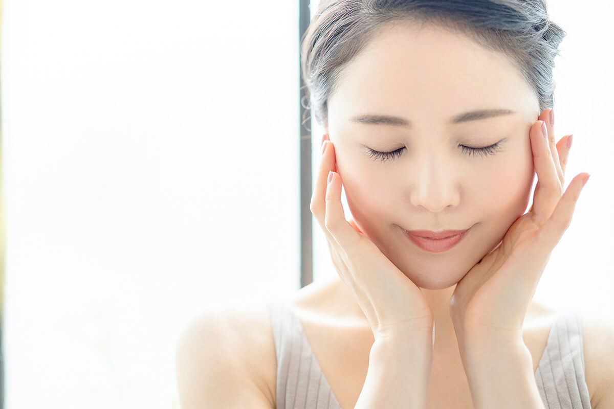 目をつむり顔に両手を添える女性